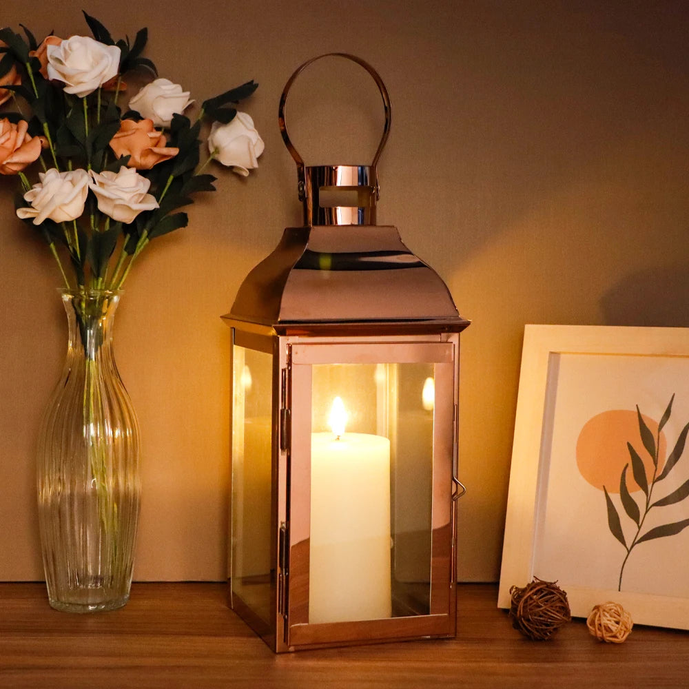 Laterne in Roségold mit Kerzenschein auf Holzregal neben Glasvase und Bild am Abend