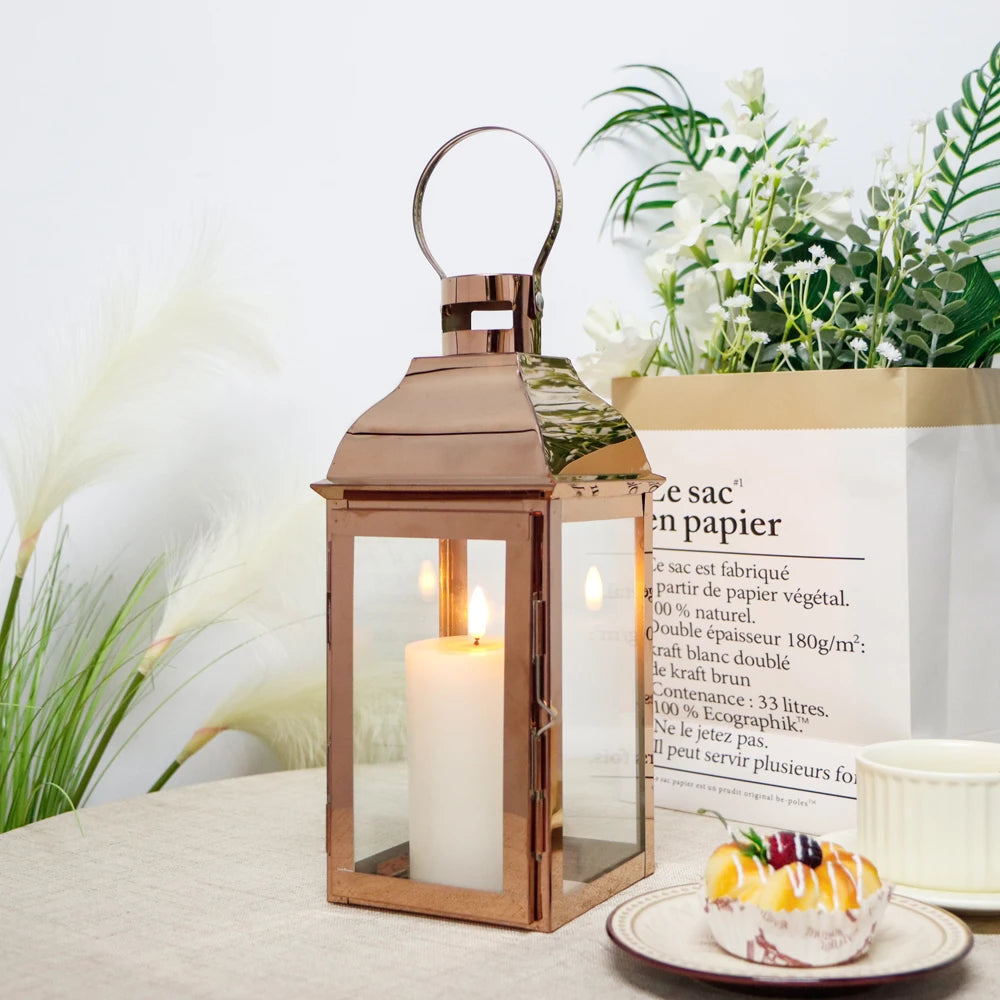 Windlicht-Laterne in Roségold mit Kerze neben Dessertteller und Grünpflanze