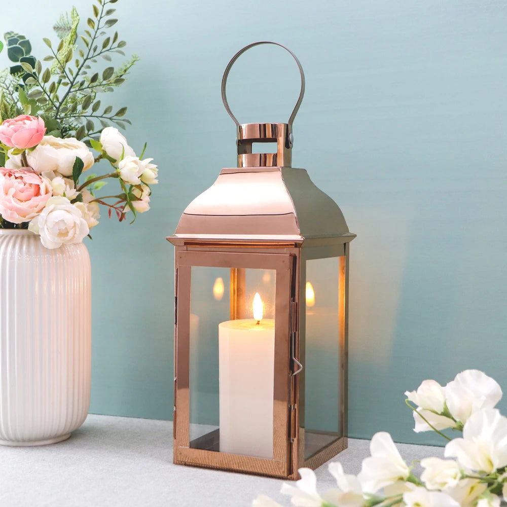 Kerzenlaterne in Roségold mit Kerze neben weißer Vase mit Rosen vor türkisfarbener Wand