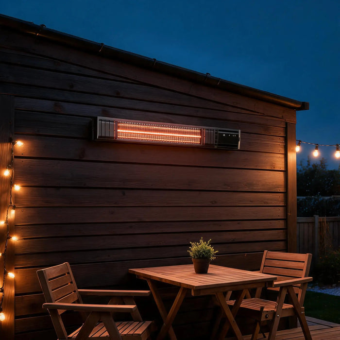 Infrarot-Heizstrahler an dunkler Holzwand über Terrassentisch mit zwei Stühlen, Lichterkette am Abend