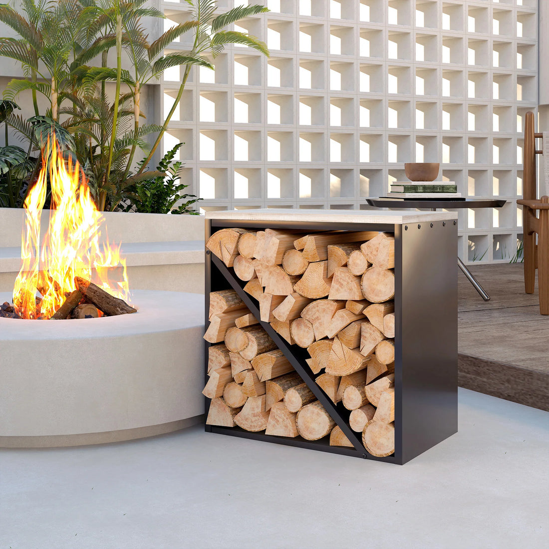 Brennholzwürfel aus Stahl mit Holzscheiten auf einer hellen Terrasse neben einer brennenden Feuerschale
