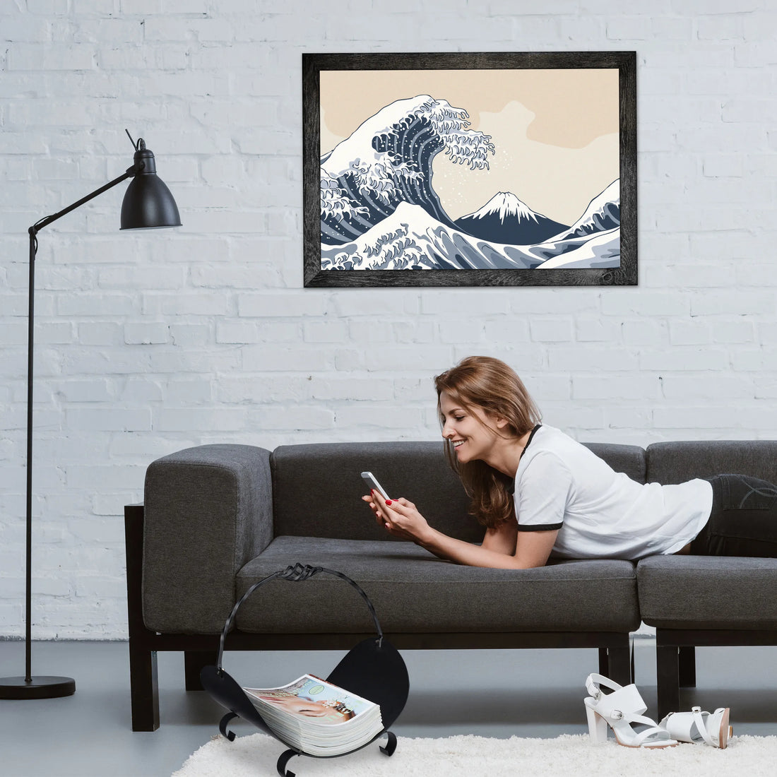 Brennholzkorb mit Zeitschriften neben einem Sofa im Wohnzimmer, eine Frau liest am Handy